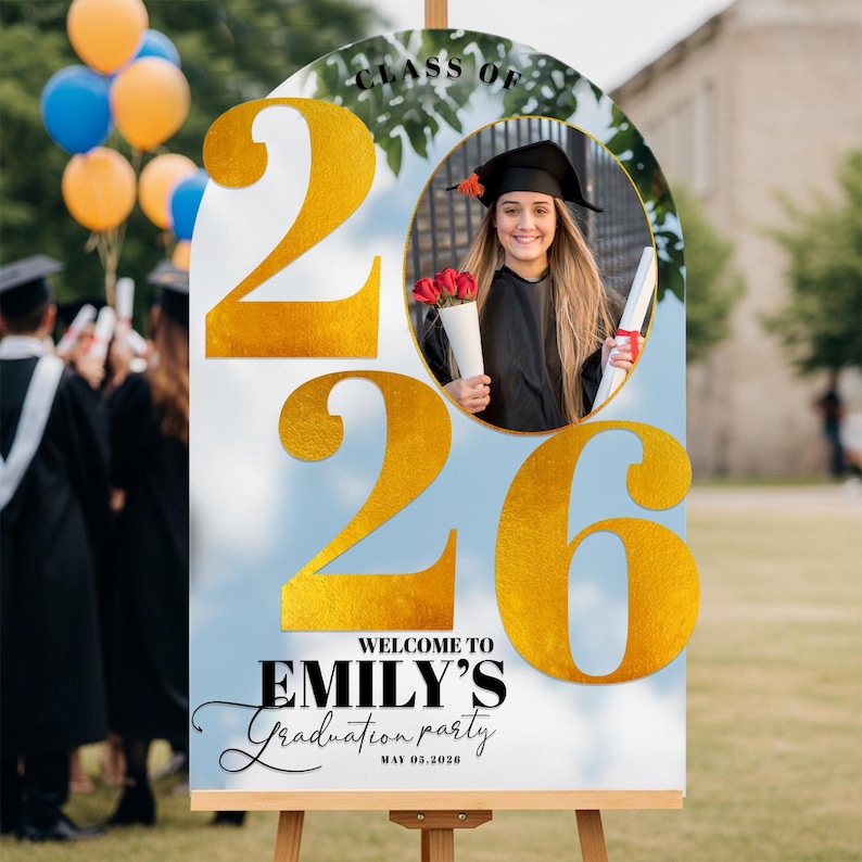May include: A graduation party sign on an easel. The sign features the text "Class of 2026" and "Welcome to Emily's Graduation Party". A photo of a graduate is in the center. Gold numbers and text are on a blue background.