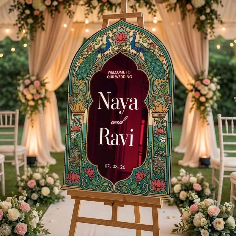 K&ouml;nnte beinhalten: Ein bogenf&ouml;rmiges Hochzeitsschild mit dunkelburgunderfarbener Mitte und wei&szlig;em Text Welcome to our wedding Naya and Ravi 07.08.26. Der Rahmen ist mit einer Bord&uuml;re im Buntglasstil verziert, die blaue Pfaue, Lotusblumen und goldene Akzente zeigt.