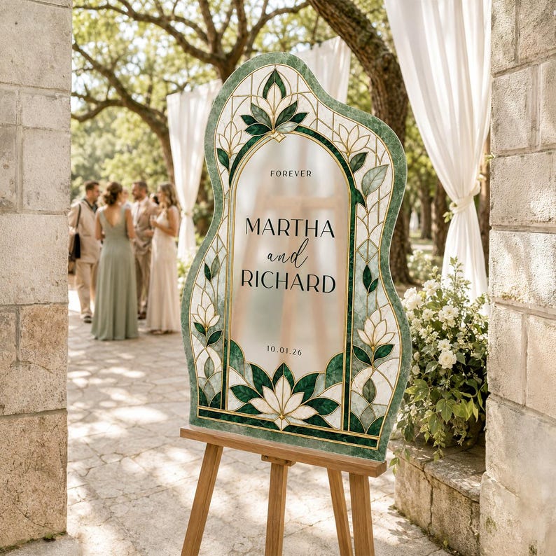 May include: An arched wedding sign with a green and white stained glass-style border featuring floral motifs. The center is frosted with the text FOREVER MARTHA and RICHARD 10.01.26 in black lettering. The sign is displayed on a wooden easel.