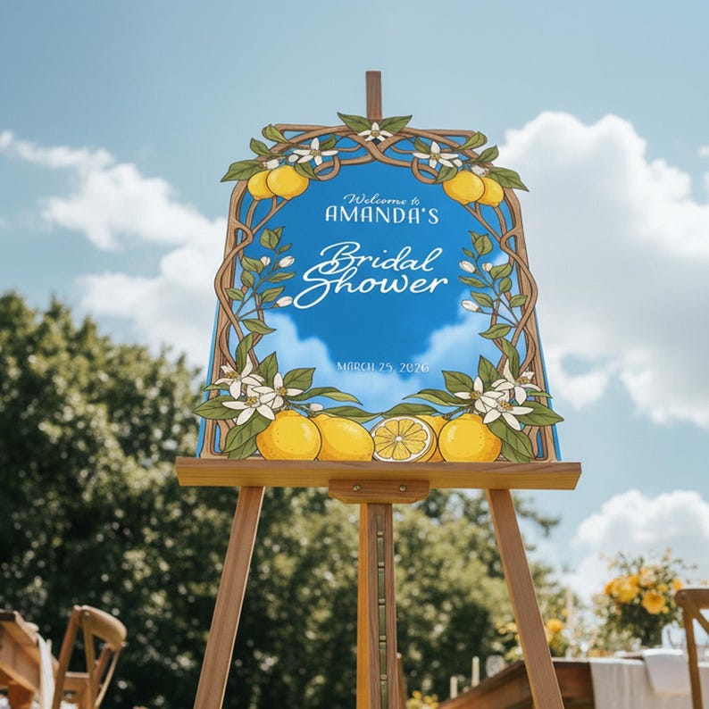 May include: A wooden easel displays a sign for "Amanda's Bridal Shower." The sign features a blue background with lemons, white flowers, and the date March 25, 2026. The sign is framed with a decorative border.