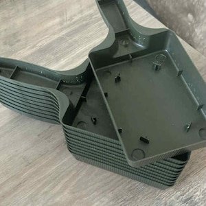 Op de afbeelding: Een stapel donkergroene plastic plantenbakken, met een handvat en een rechthoekige basis. De bakken zijn ontworpen voor het planten en tuinieren. De bakken zijn gestapeld op een houten oppervlak.