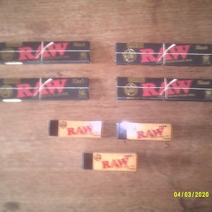 May include: Four packs of RAW rolling papers, each with a white string tied around them. Three individual packs of RAW rolling papers are also shown.