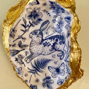 May include: A gold-leafed oyster shell with a blue and white floral design featuring a rabbit and butterflies.