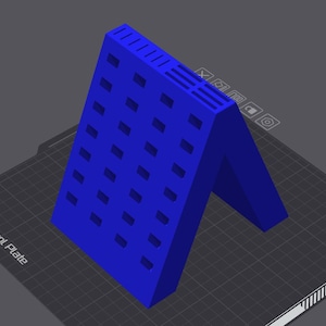 Op de afbeelding: Een helderblauw, 3D-geprint object met een uniek architectonisch ontwerp. De structuur heeft een reeks rechthoekige uitsparingen en horizontale lijnen aan de bovenkant. Het object staat tegen een donkergrijze achtergrond.