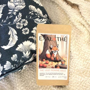May include: A brown paper bag with a cartoon fox illustration and the text "EXAL THE" and "THE VERT POMME GRILLÉE". The bag contains a green tea blend with apple, raisin, and rose.