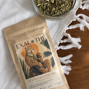 May include: A brown paper pouch of Exal Thé Détox Amazonienne loose leaf tea featuring a leopard illustration and a clear glass bowl filled with green tea leaves and dried fruit pieces, showcasing ingredients like maté, pineapple, and mango.