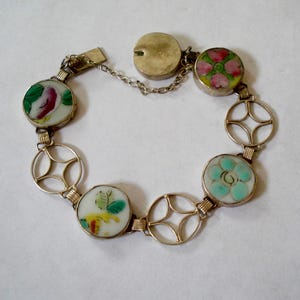 May include: A link bracelet featuring alternating circular charms and openwork metal geometric components. The charms display hand-painted floral motifs in shades of pink, green, yellow, and turquoise on a white background. It includes a metal clasp.