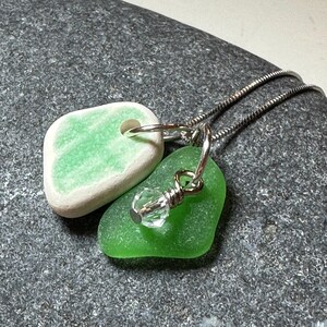 May include: A silver chain necklace with two green glass pendants. One pendant is a smooth, rounded shape with a white edge. The other pendant is a more irregular shape with a clear crystal bead.
