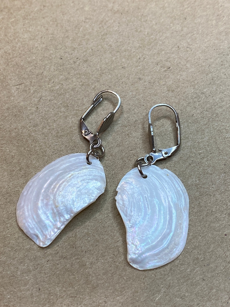 以下が含まれることがあります： 銀色のレバーバック留め具が付いた、白い虹色の貝殻のイヤリングのペアです。