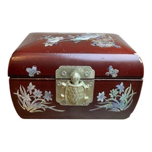 May include: A rectangular dark brown wooden box featuring iridescent mother-of-pearl floral and butterfly inlays on the lid and front. The box is secured with a metallic latch shaped like a turtle, centered on the front panel of the container.
