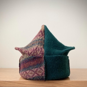 May include: A distinctive two-tone hat. One side is patterned with purple, blue, and tan hues, while the other is a solid teal green. The hat is displayed on a wooden surface.