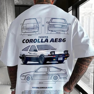 May include: White t-shirt with a Toyota Corolla AE86 design. The print includes car schematics, a detailed car illustration, and the text "TOYOTA COROLLA AE86". The shirt has a crew neck and short sleeves.