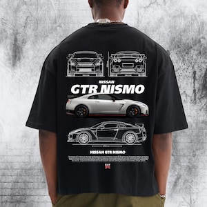 May include: A black t-shirt featuring a white graphic print of a Nissan GTR Nismo. The design includes front and rear technical line drawings, a side-profile image of the white car, the text NISSAN GTR NISMO, and a paragraph of descriptive text.