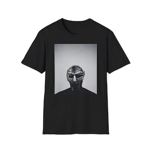 以下が含まれることがあります： 銀色のマスクをつけた人のグラフィックプリントが施された黒いTシャツ