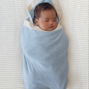 Un bébé emmailloté dans notre couverture en cachemire Botiboty. la couverture mesure 80x100cm et permet de tenir au chaud à la maison, en extérieur. le cachemire est une matière idéale pour la peau de bébé. Idéal pour un joli cadeau de naissance