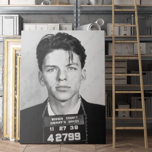 May include: Black and white mugshot of a man with short dark hair. The mugshot has a name tag that reads "Bergen County Sheriff's Office" and the numbers "11 27 38 42799".