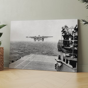 May include: A black and white photograph of a bomber plane taking off from an aircraft carrier. The plane is flying over the ocean, and there are people on the deck of the carrier watching it take off.