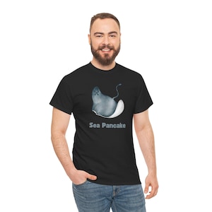 Pode incluir: Uma camiseta preta com um gráfico de uma arraia cinza e branca com o texto "Sea Pancake" impresso abaixo da imagem.