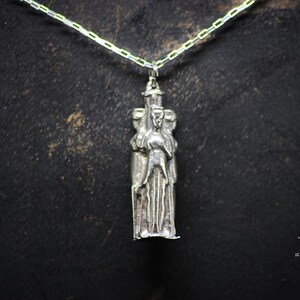 May include: Silver pendant necklace featuring a detailed sculpture of three figures standing close together. The figures are stylized and appear to be wearing robes.