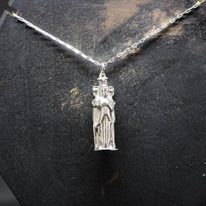 May include: Silver necklace with a pendant featuring a three-dimensional sculpture of three figures standing together.