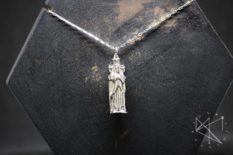 May include: Silver necklace with a pendant featuring a three-dimensional sculpture of three figures standing together.