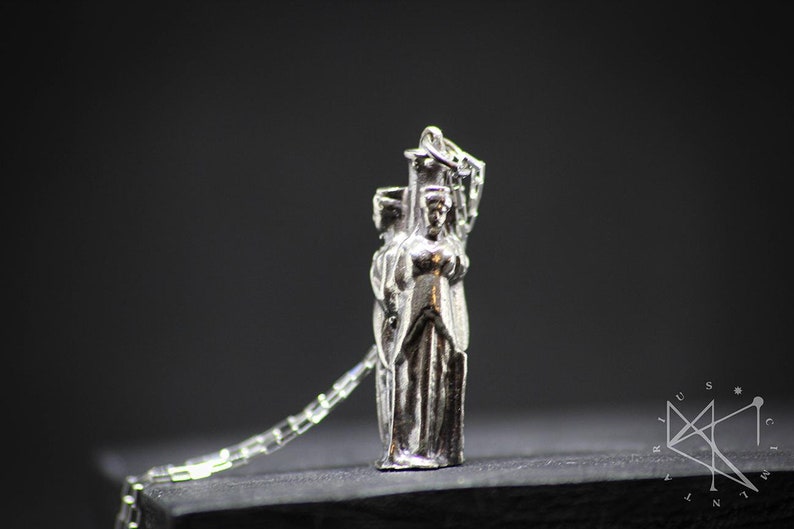 May include: Silver pendant necklace featuring a detailed sculpture of three figures standing together. The figures are wearing long robes and appear to be in a procession.