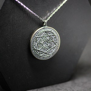 Puede incluir: Un collar de cadena de plata con un colgante redondo que presenta un dise&ntilde;o detallado e intrincado de una estrella de seis puntas rodeada por un c&iacute;rculo de texto.