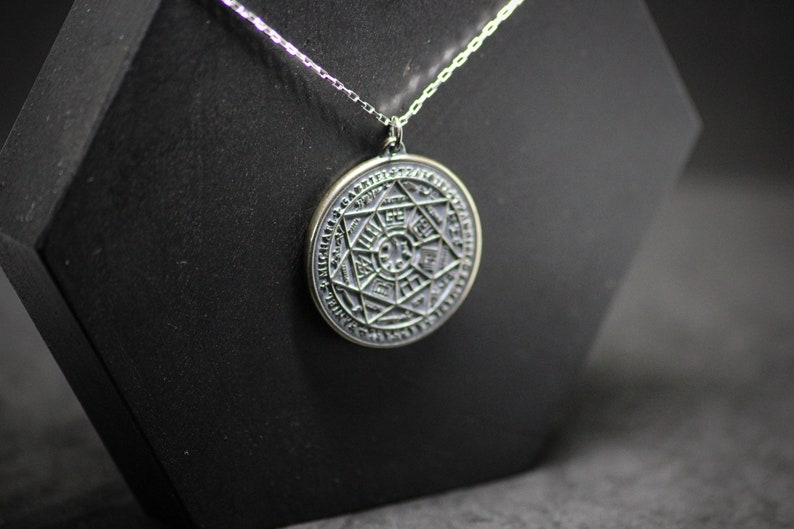 Puede incluir: Un collar de cadena de plata con un colgante redondo que presenta un dise&ntilde;o detallado e intrincado de una estrella de seis puntas rodeada por un c&iacute;rculo de texto.