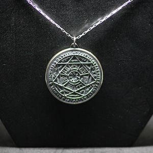 Puede incluir: Un collar de plata con un colgante redondo que presenta un dise&ntilde;o detallado e intrincado de una estrella con un c&iacute;rculo en el centro y texto alrededor del per&iacute;metro.