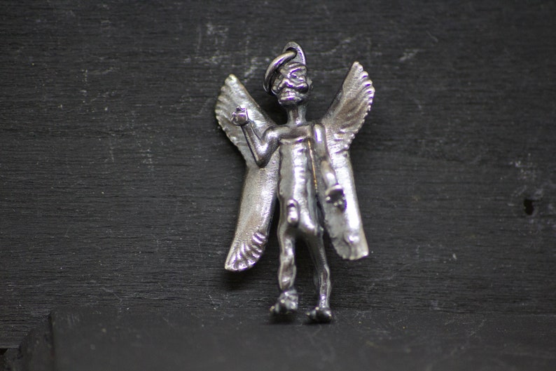 May include: A silver angel pendant with wings and a detailed face. The angel is standing with its arms outstretched.