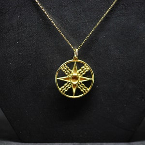 Op de afbeelding: Een gouden ketting met een hanger met een gestileerde achtpuntige ster omringd door een cirkel van golven.
