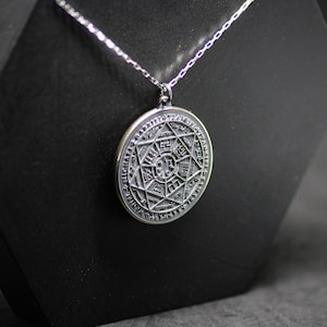 Puede incluir: Un collar de plata con un colgante redondo que presenta un dise&ntilde;o grabado detallado de una estrella dentro de un c&iacute;rculo. El colgante tiene una cadena de plata.
