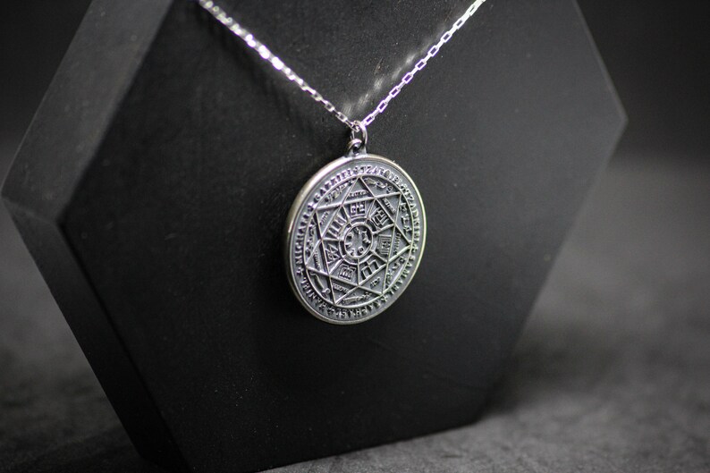 Puede incluir: Un collar de plata con un colgante redondo que presenta un dise&ntilde;o grabado detallado de una estrella dentro de un c&iacute;rculo. El colgante tiene una cadena de plata.