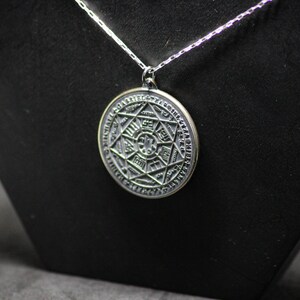 Puede incluir: Un collar de plata con un colgante redondo que presenta un dise&ntilde;o detallado e intrincado de una estrella dentro de un c&iacute;rculo. El colgante est&aacute; grabado con s&iacute;mbolos y caracteres.