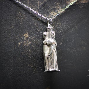 May include: Silver pendant necklace featuring a three-dimensional sculpture of three figures standing together.