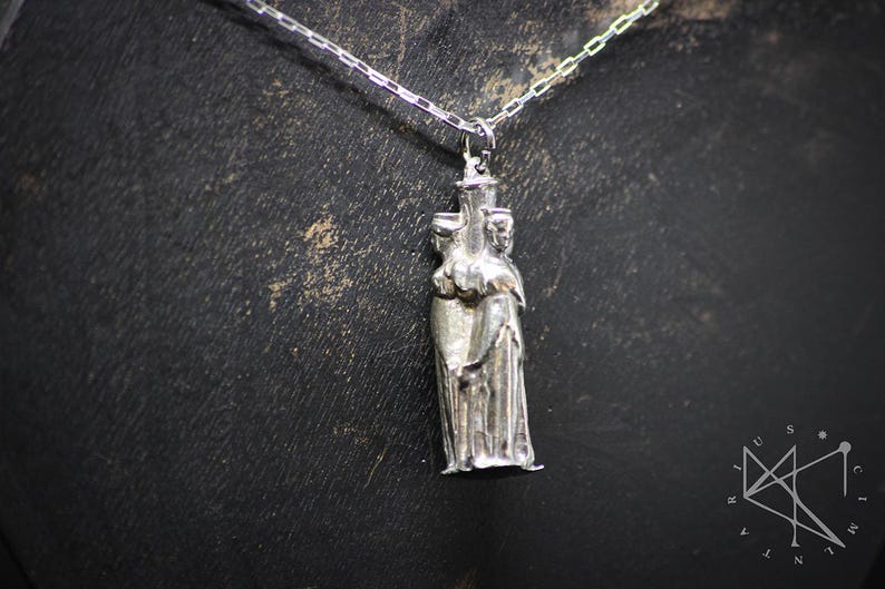 May include: Silver pendant necklace featuring a three-dimensional sculpture of three figures standing together.