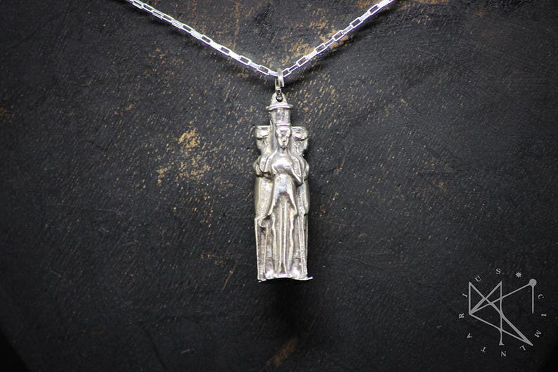 May include: Silver pendant necklace featuring a detailed sculpture of three figures standing together. The figures are wearing long robes and have intricate facial features.