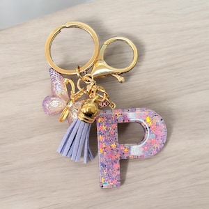 May include: A purple glitter letter P keyring with a gold chain, a purple tassel, and a butterfly charm.