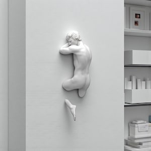 Könnte beinhalten: Eine weiße Wandskulptur, die eine liegende menschliche Figur darstellt. Die Skulptur ist an einer weißen Wand befestigt, wobei der Oberkörper und das untere Bein abgetrennt sind. Die Skulptur ist ein minimalistisches Kunstwerk.
