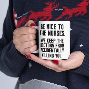 May include: White ceramic coffee mug with black text that reads "Be nice to the nurses. We keep the doctors from accidentally killing you."
