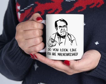 May include: White ceramic mug featuring a black and white illustration of a man with glasses and a stethoscope. The mug has the text "DO YOU LOOK LIKE YOU ARE MALNOURISHED?"