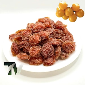 Puede incluir: Un plato blanco lleno de ciruelas pasas. Las ciruelas pasas son de un color marrón rojizo oscuro y tienen una textura arrugada. Un pequeño racimo de ciruelas frescas, de color amarillo dorado, se encuentra en la esquina superior derecha.