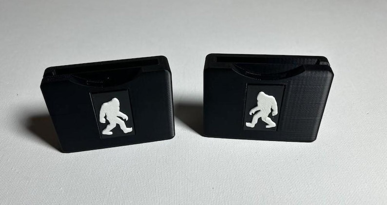 May include: Two black plastic cases with a white silhouette of a Bigfoot walking on each case.