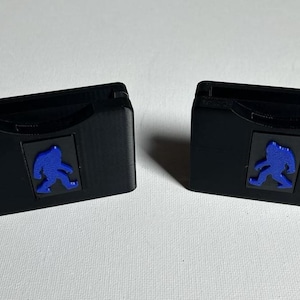May include: Two black plastic cases with a blue silhouette of a person walking on each. The cases are designed to hold game cartridges.