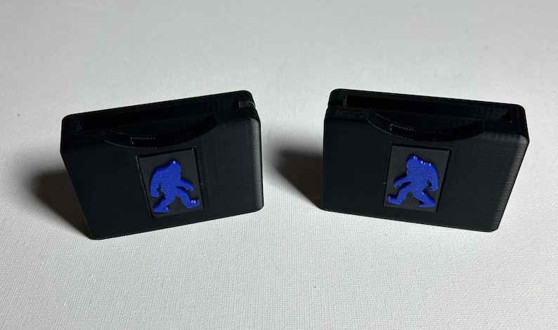 May include: Two black plastic cases with a blue silhouette of a person walking on each. The cases are designed to hold game cartridges.