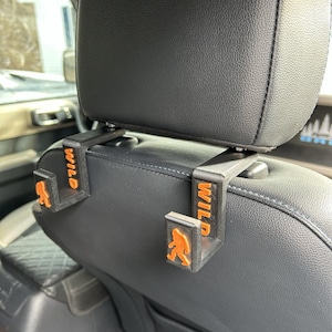 May include: Two black plastic car seat headrest hooks with an orange silhouette of a Bigfoot and the word "WILD" printed on each hook.