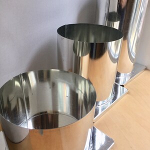 May include: Three silver metal candle molds of different sizes, each with a square base. The molds are arranged in a row from largest to smallest.