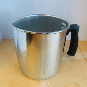 May include: A silver stainless steel jug with a black handle. The jug is empty and sitting on a wooden surface.