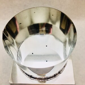 May include: A silver metal candle mold with a round top and a square base. The mold has three small holes in the bottom.