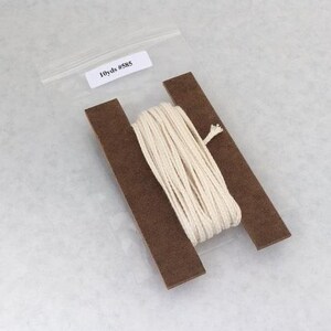May include: A spool of white cotton cord, wrapped around two brown cardboard pieces, with a label that reads "10yds #585".